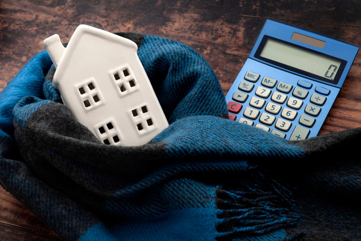 Ceramic house and calculator wrapped in a scarf. Save on heating bills with plumbing upgrades