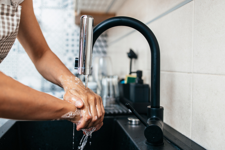 Young adult woman washing her hands on kitchen sink. Household and home and personal hygiene routine.
